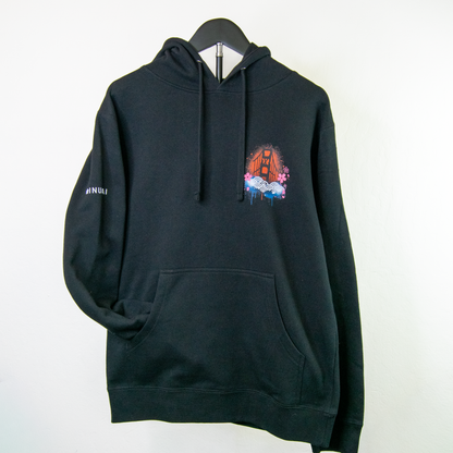 A black pullover hoodie hanging on a black hanger against a plain white wall. The hoodie features a colorful graphic print on the left chest depicting a bridge with graffiti-style paint drips, and the word 'Inurai' printed in white on the right sleeve.