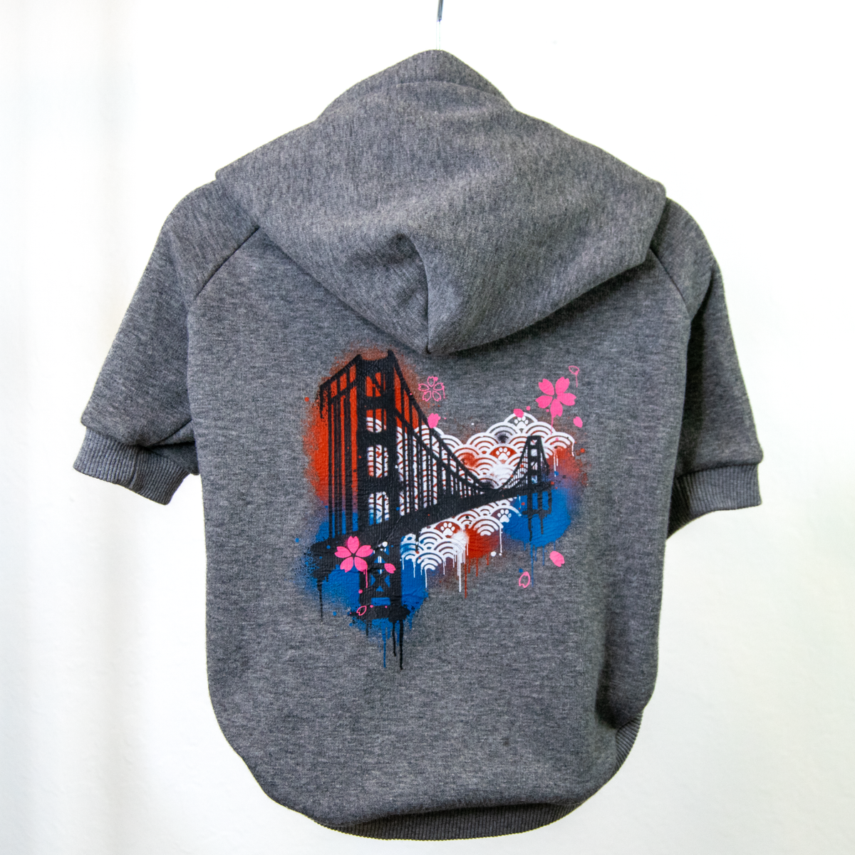 A gray heathered pet hoodie shown from the back, featuring a colorful graphic print of the Golden Gate Bridge with pink flowers and blue and white wave patterns.
