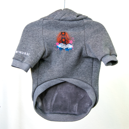 A gray heather pet hoodie with a short-sleeve design, shown hanging against a plain white background. The sweater features a colorful graphic of the Golden Gate Bridge with waves, and the left sleeve has the word 'INURAI' printed in white.