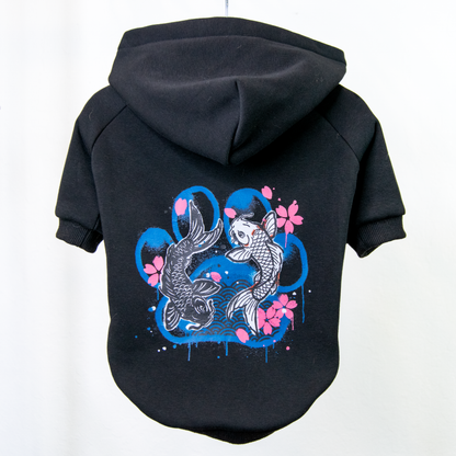 A black pet hoodie shown from the back, featuring a graphic print of two koi fish, pink cherry blossoms, and blue paint splatters.