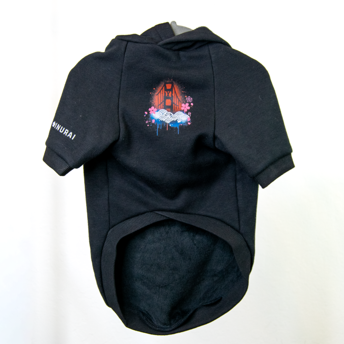 A black pet hoodie with a short-sleeve design, featuring a colorful graphic of the Golden Gate Bridge on the front with red and blue paint splatters
